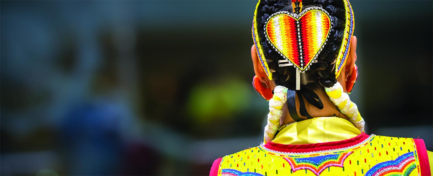 Back of an Indigenous person in regalia wearing an orange heart-shaped beaded hair-piece