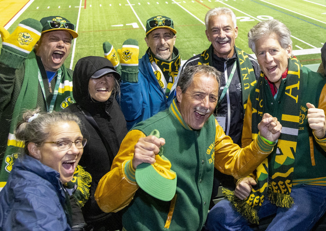 Alumni wearing green + gold cheering while watching a football game