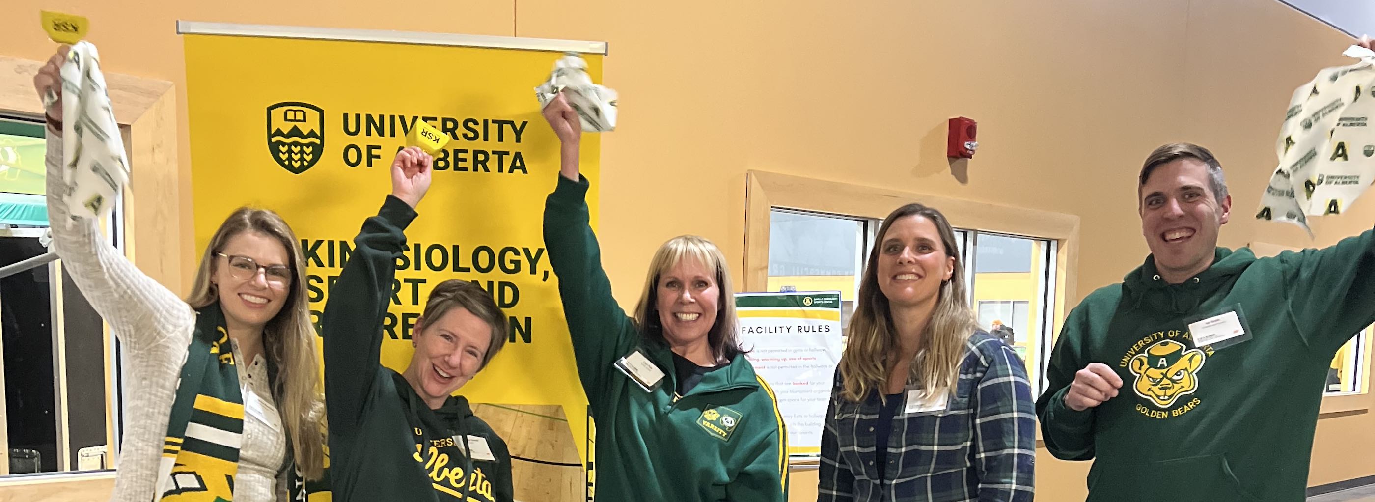 Alumni wearing the u of a green and gold colours and waving alumni swag at a Kinesiology, sport, and recreation alumni event
