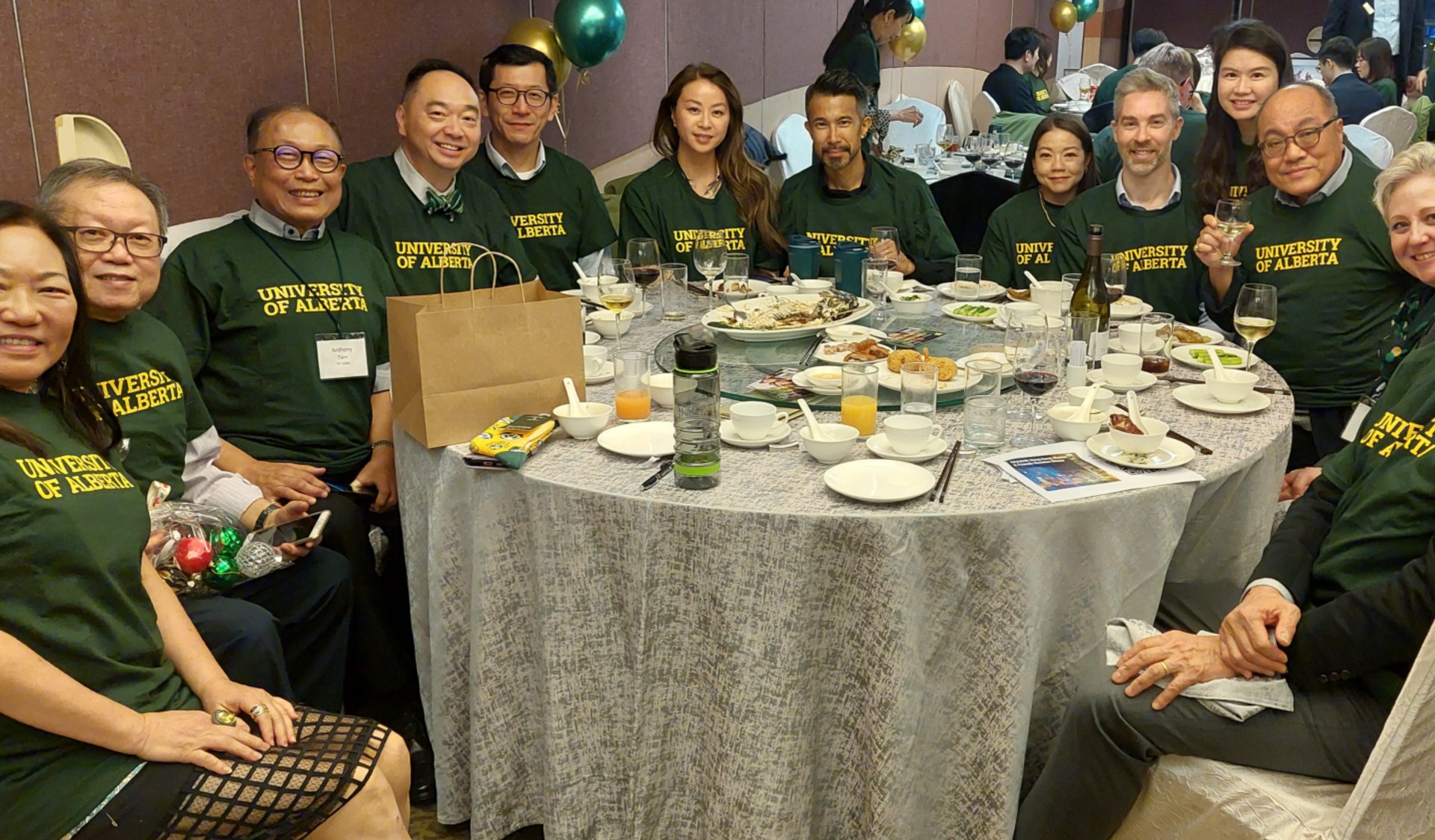 Large group of people at a dinner table wearing green and gold sweaters.