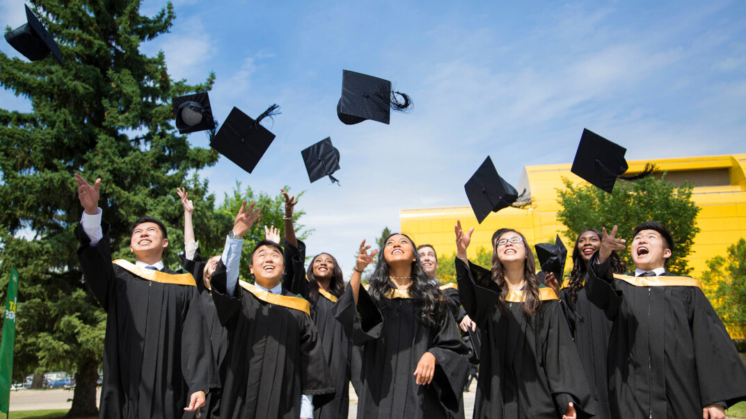 New grads throw their caps into the air on a sunny day.