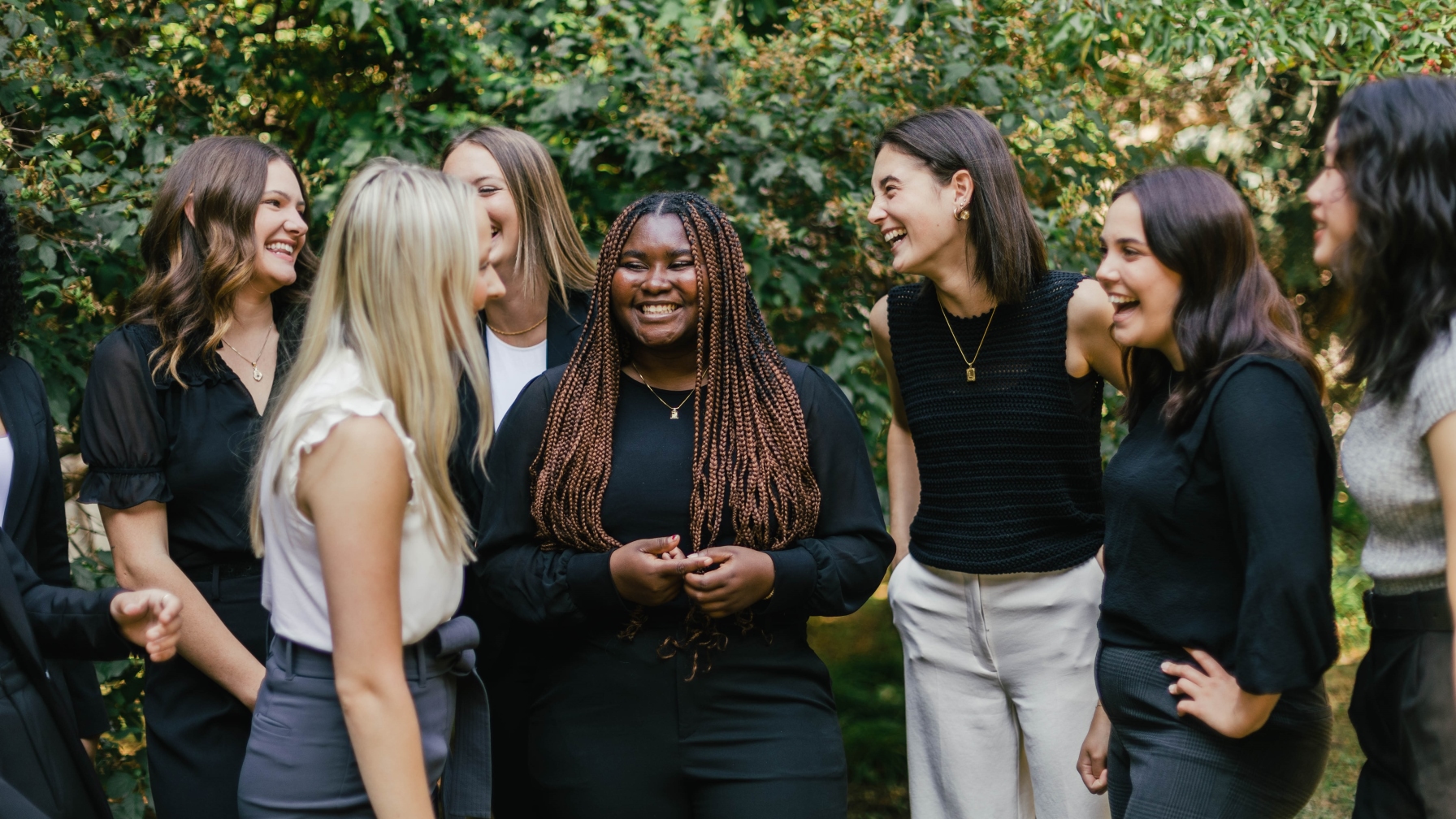 an image of a group of young women huddled together, laughing and smiling outside. 