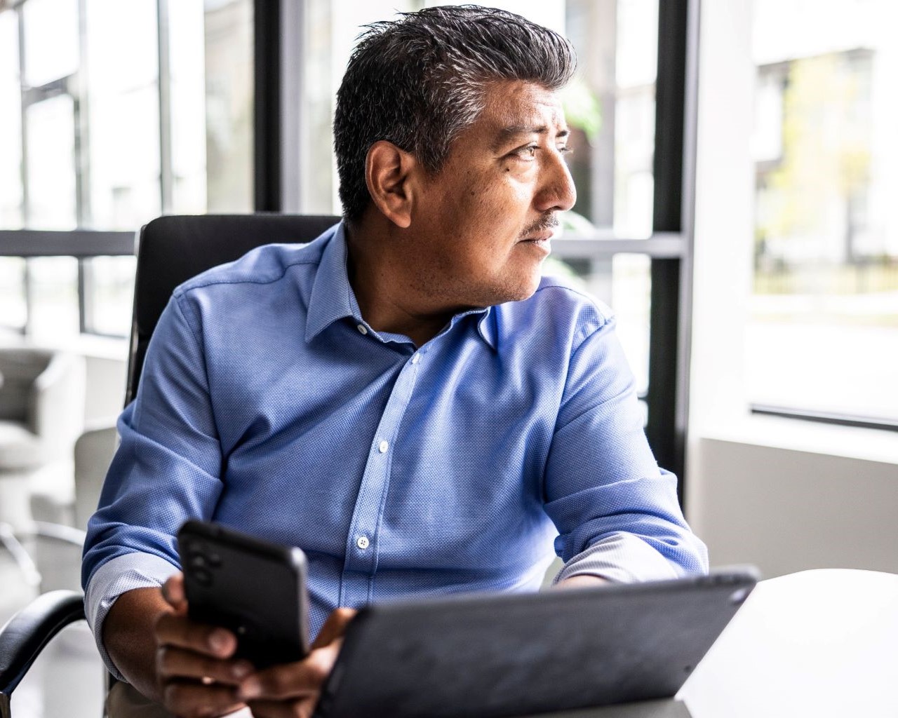 male sitting at desk with laptop and cell phone looking out window