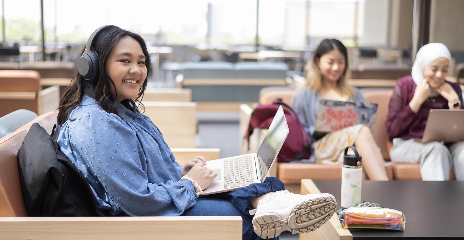 Students in studying in the fourth floor lounge studying on laptop with headphones on