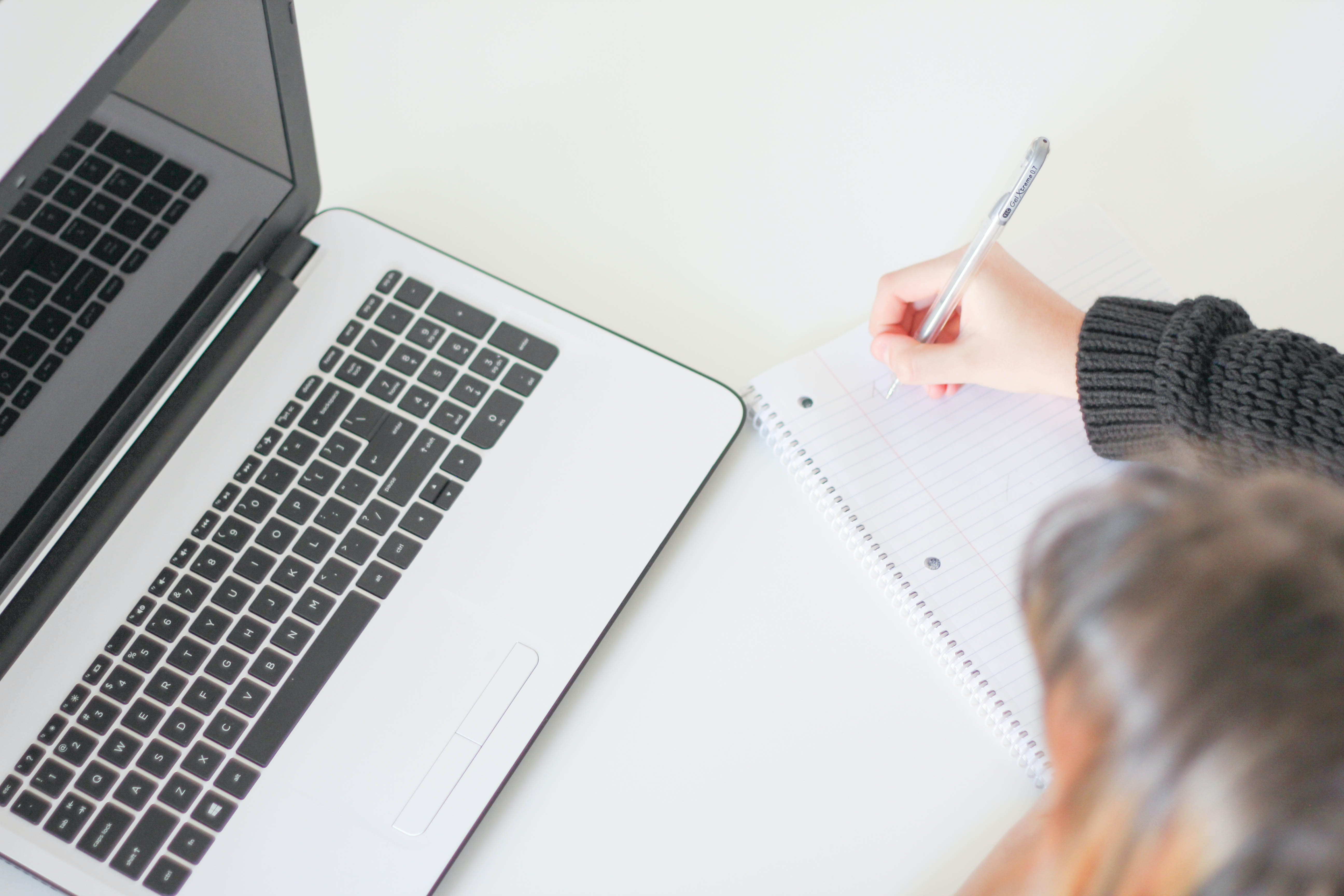 laptop on desk with person writing in a notepad