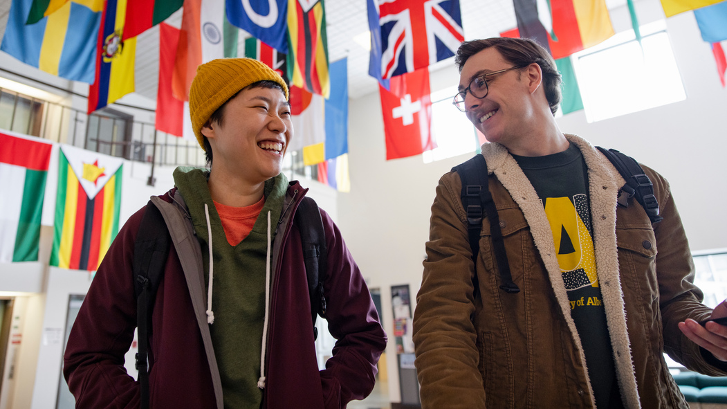 Two students laugh together under a banner of flags.