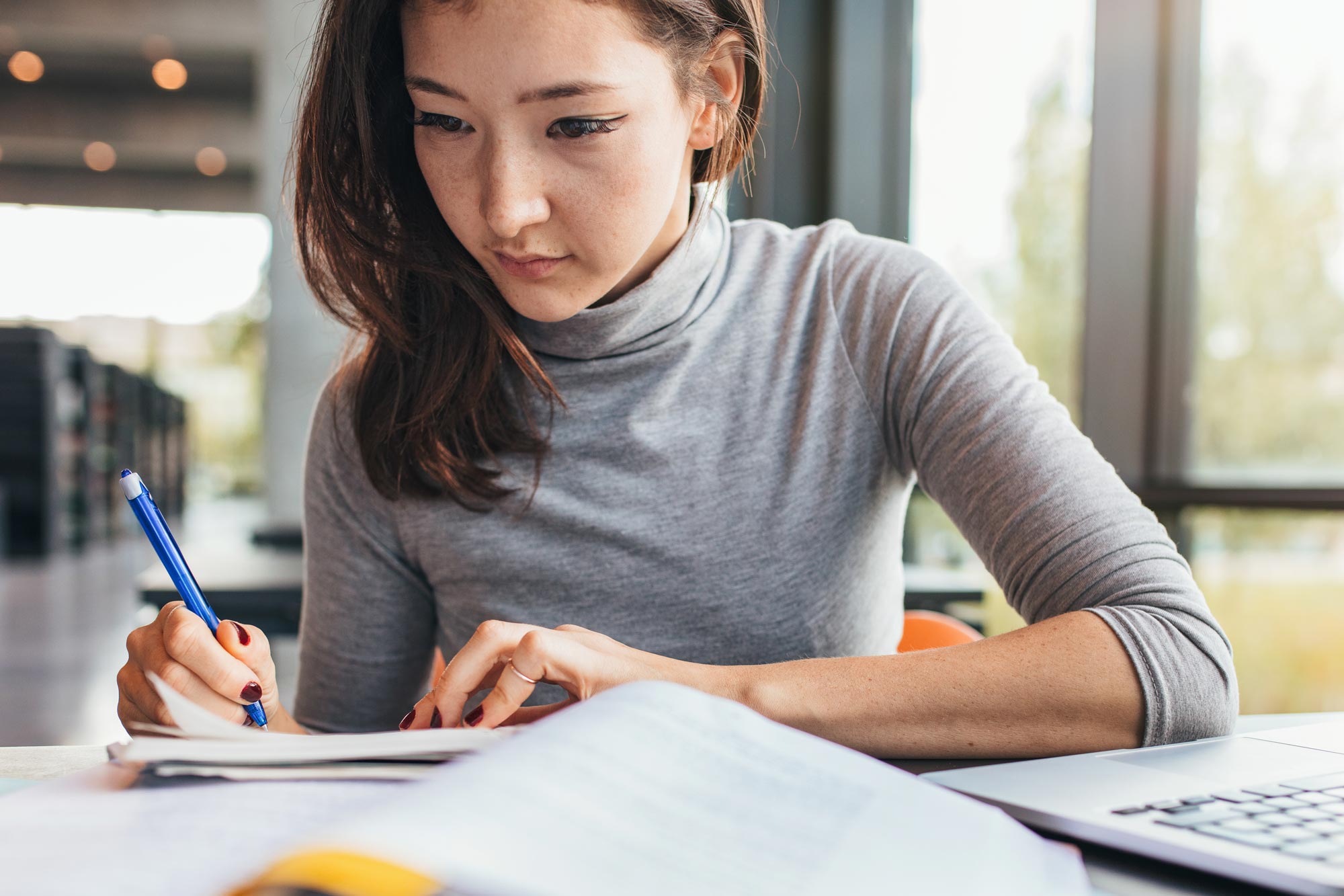 Woman writing on page next to a laptop