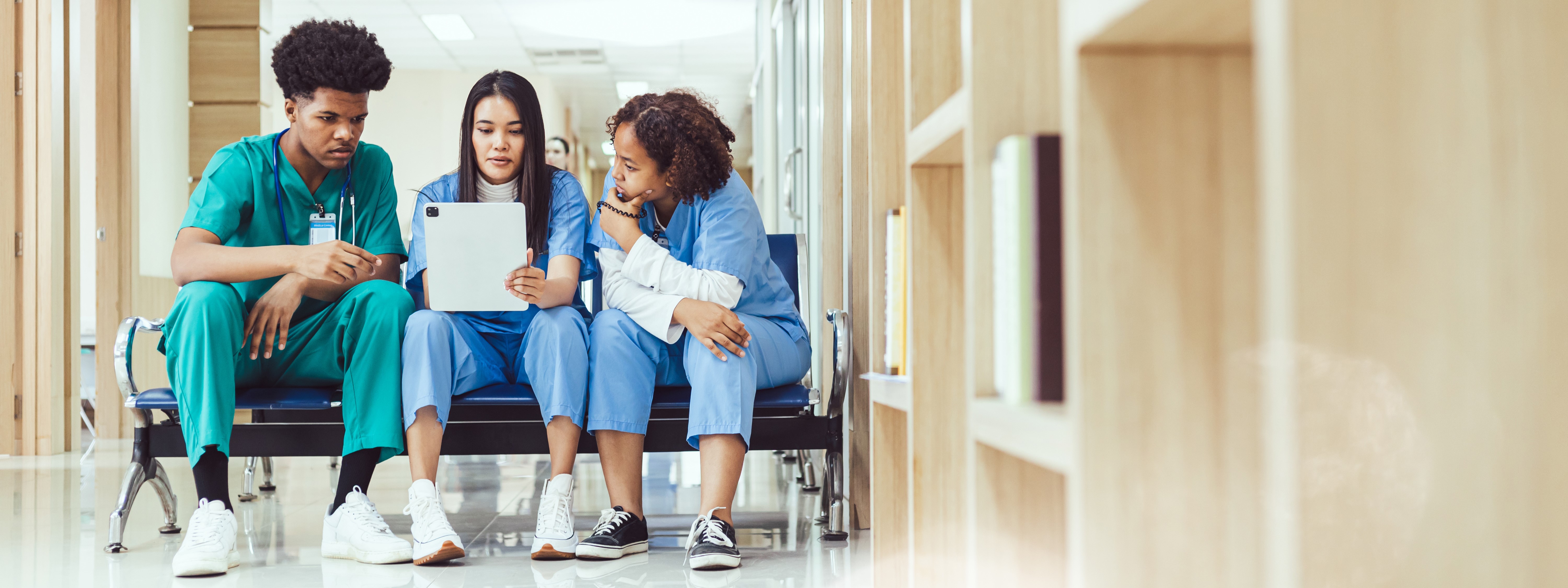 photo of three learners in scrubs sitting and looking at a notebook together