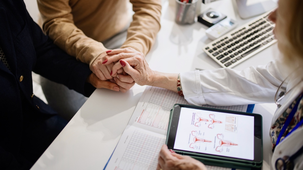 Stock image of a couple holding hands with a third hand holding the couples'. The third person is wearing a lab coat.