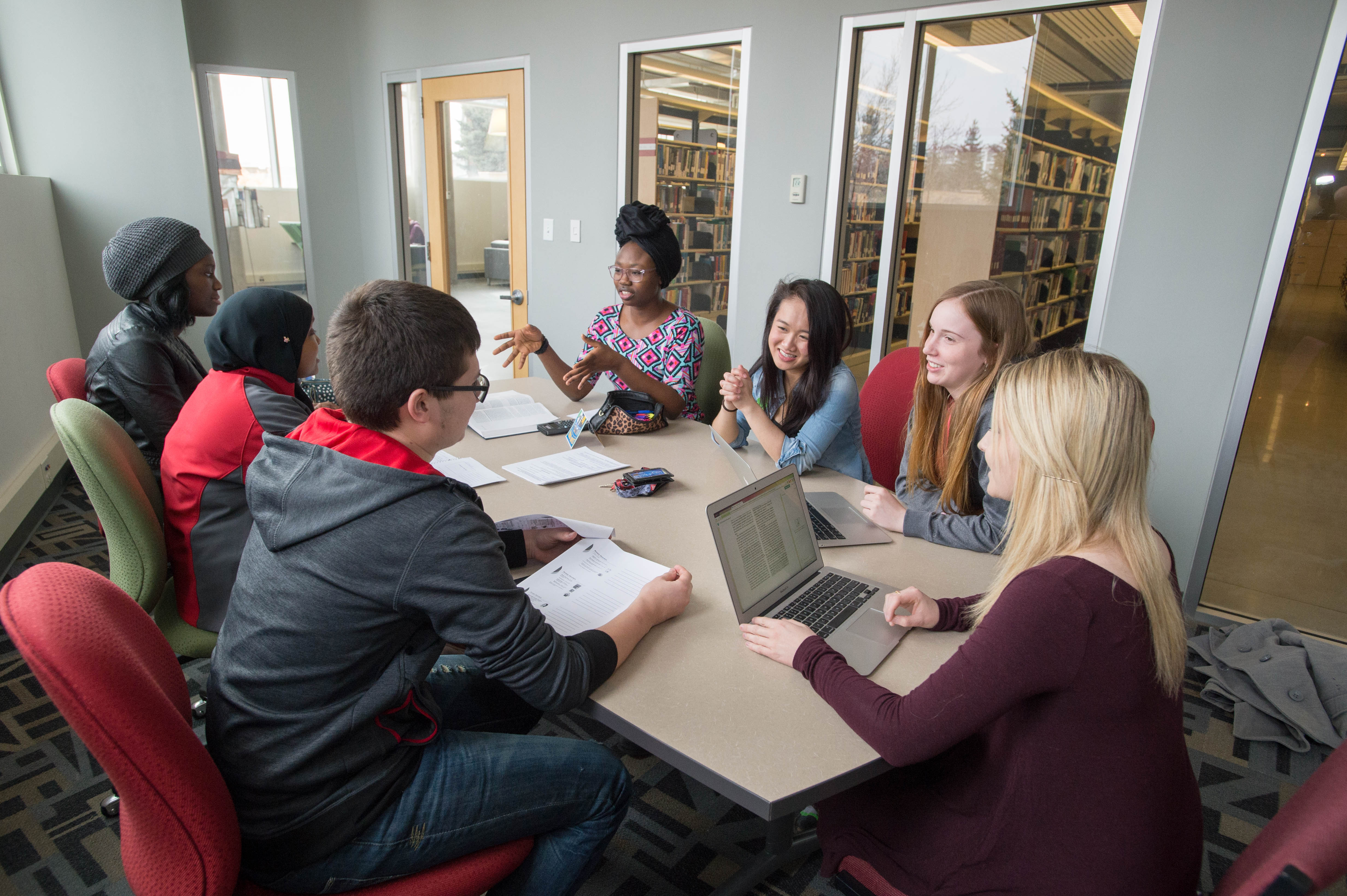 A group of student sitting at a table discussing amongst each other.