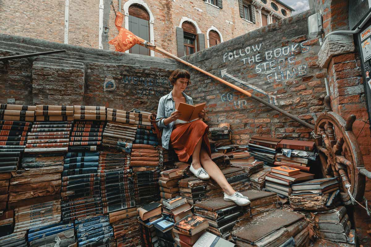 Woman reading while sitting on a pile of books made into steps